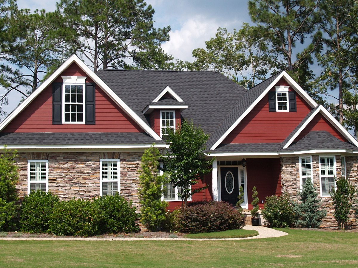 A red house with stone walls and a green lawn. The house features a black roof and white trim.