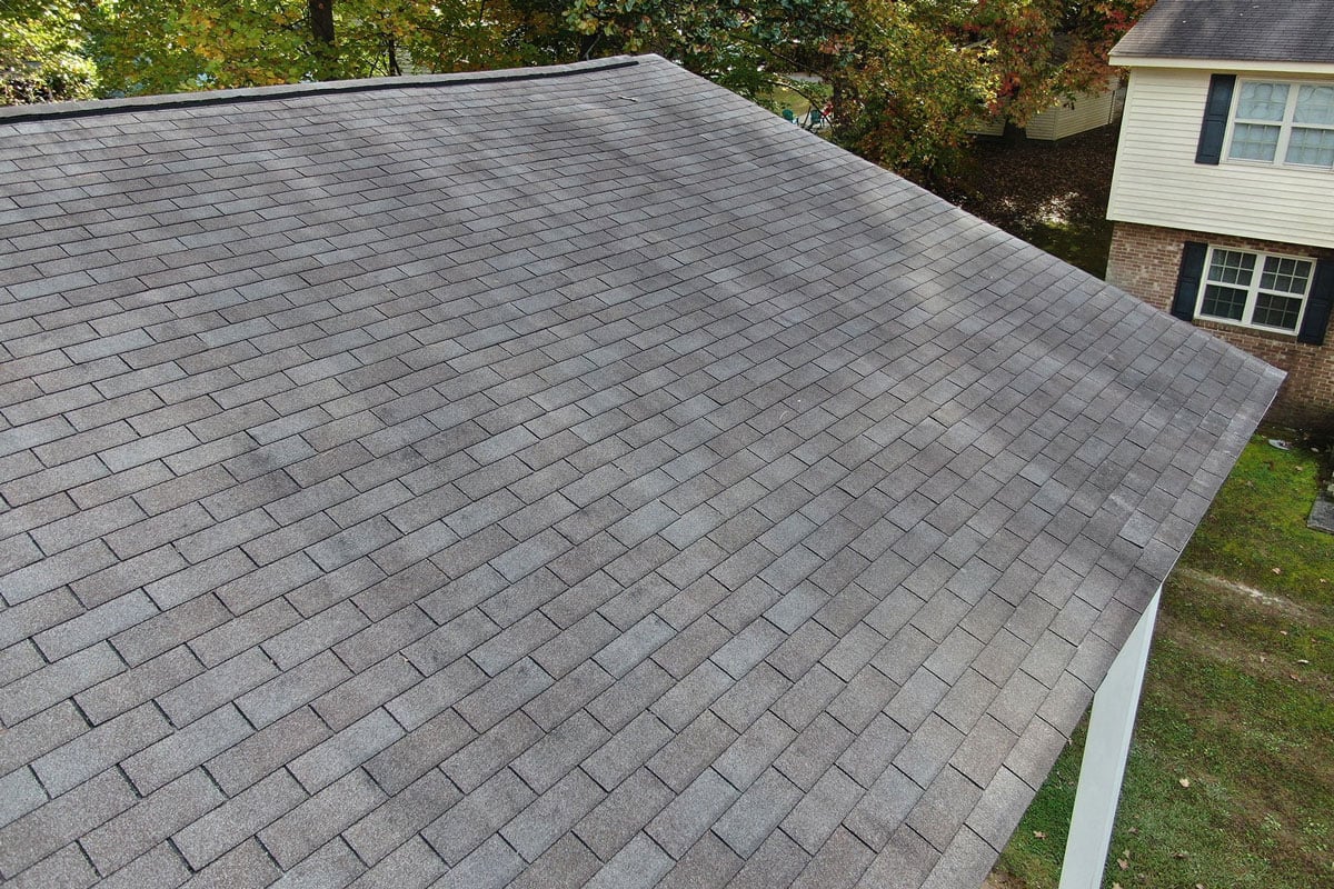 A gray shingled roof of a house with a grassy yard.