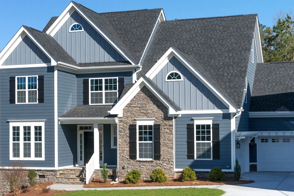 A modern two-story house with blue siding and white trim. The house has a stone front porch and a two-car garage.
