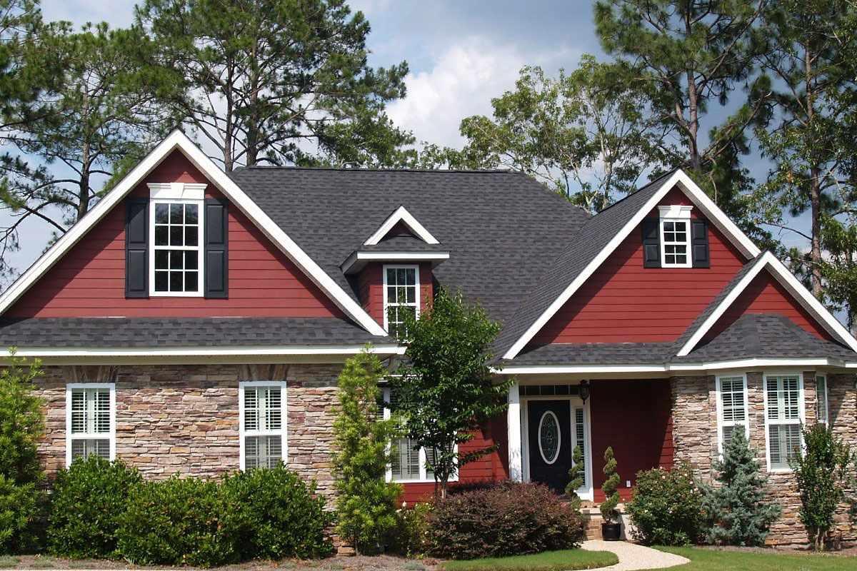 A red house with stone and white trim exterior. The house has a black roof and a front porch.