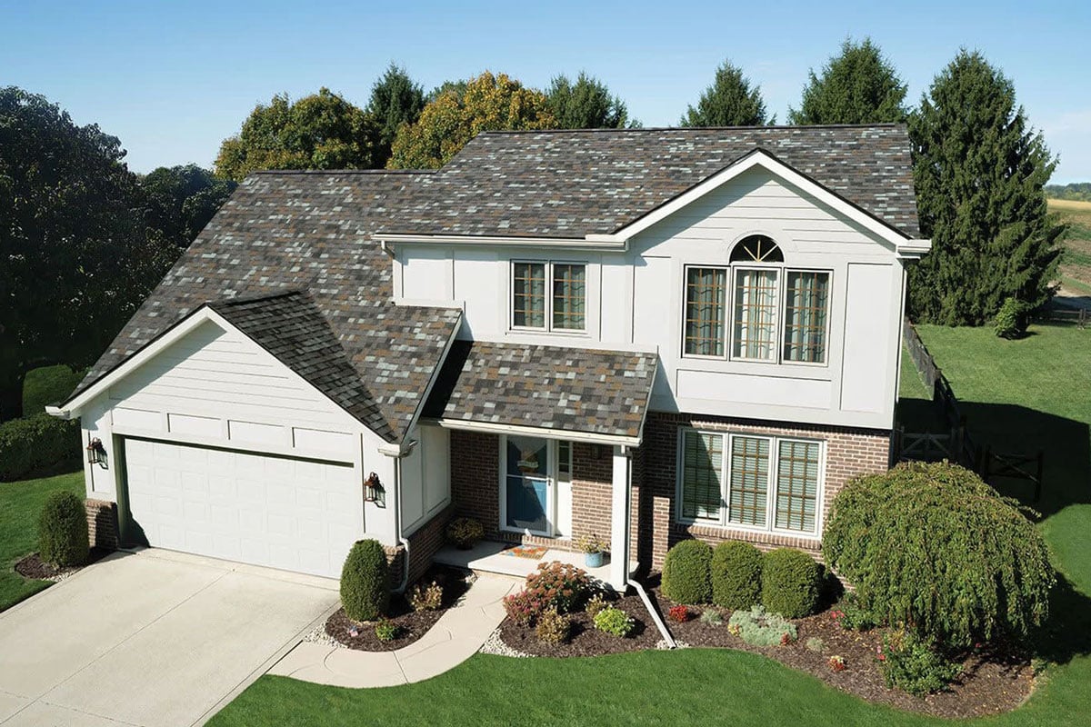 A two-story house with a white exterior and a gray roof. The house features a well-manicured lawn and shrubs.