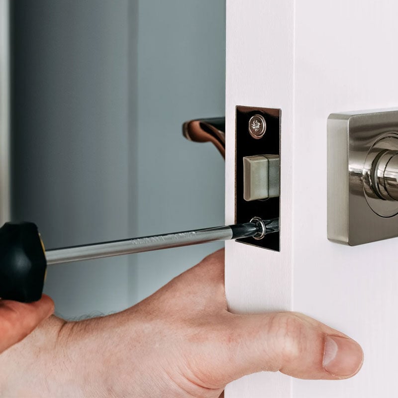 A person using a screwdriver to fix a door lock. The handyman is focused on the task.