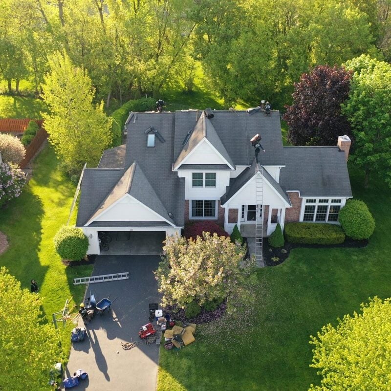 Luxury Suburban Home Aerial View A large suburban home with a well-manicured lawn. The house features a gray roof and white trim.